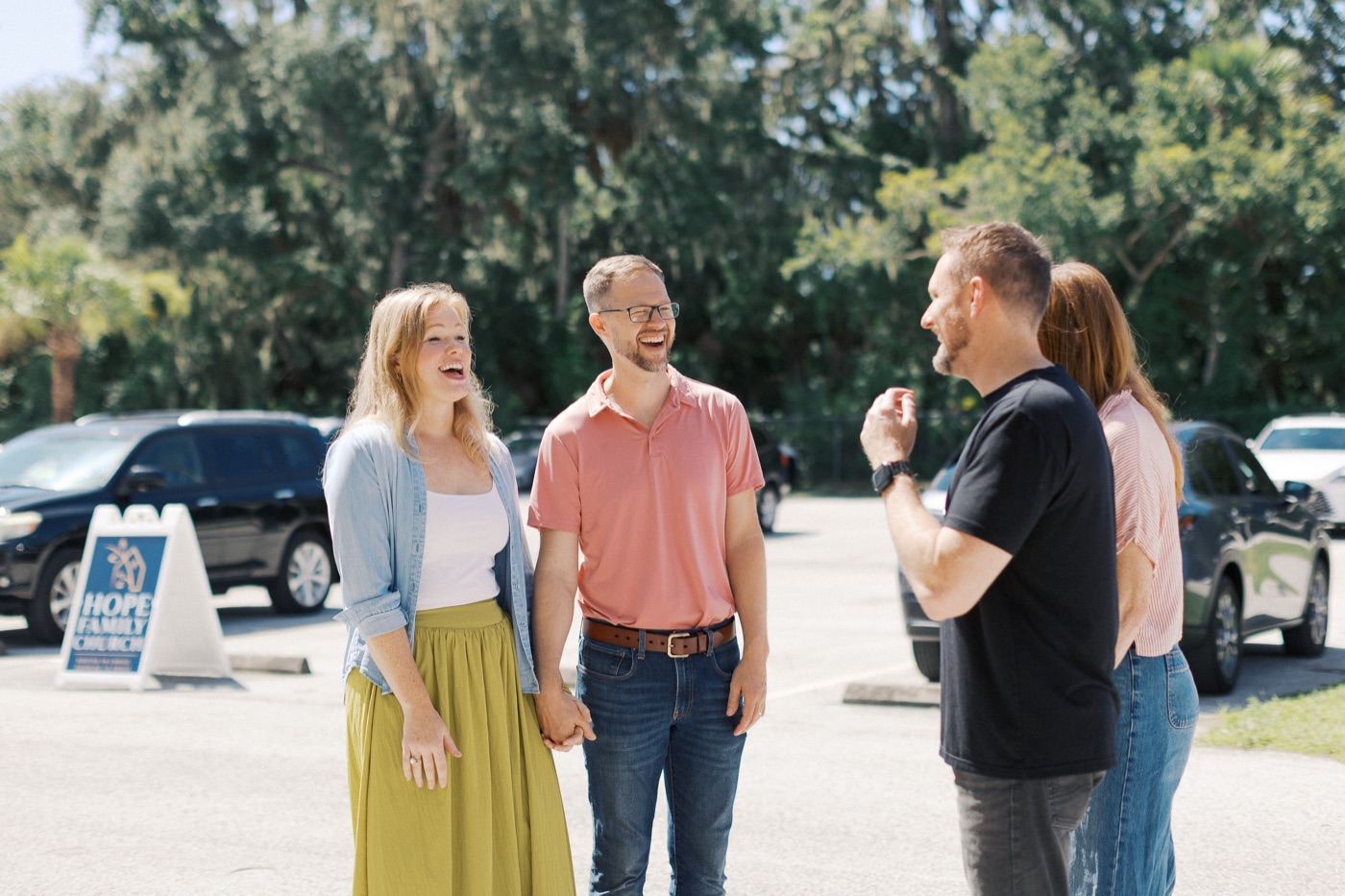 Two couples from Hope Family Church laughing together in the parking lot on a sunny Sunday morning