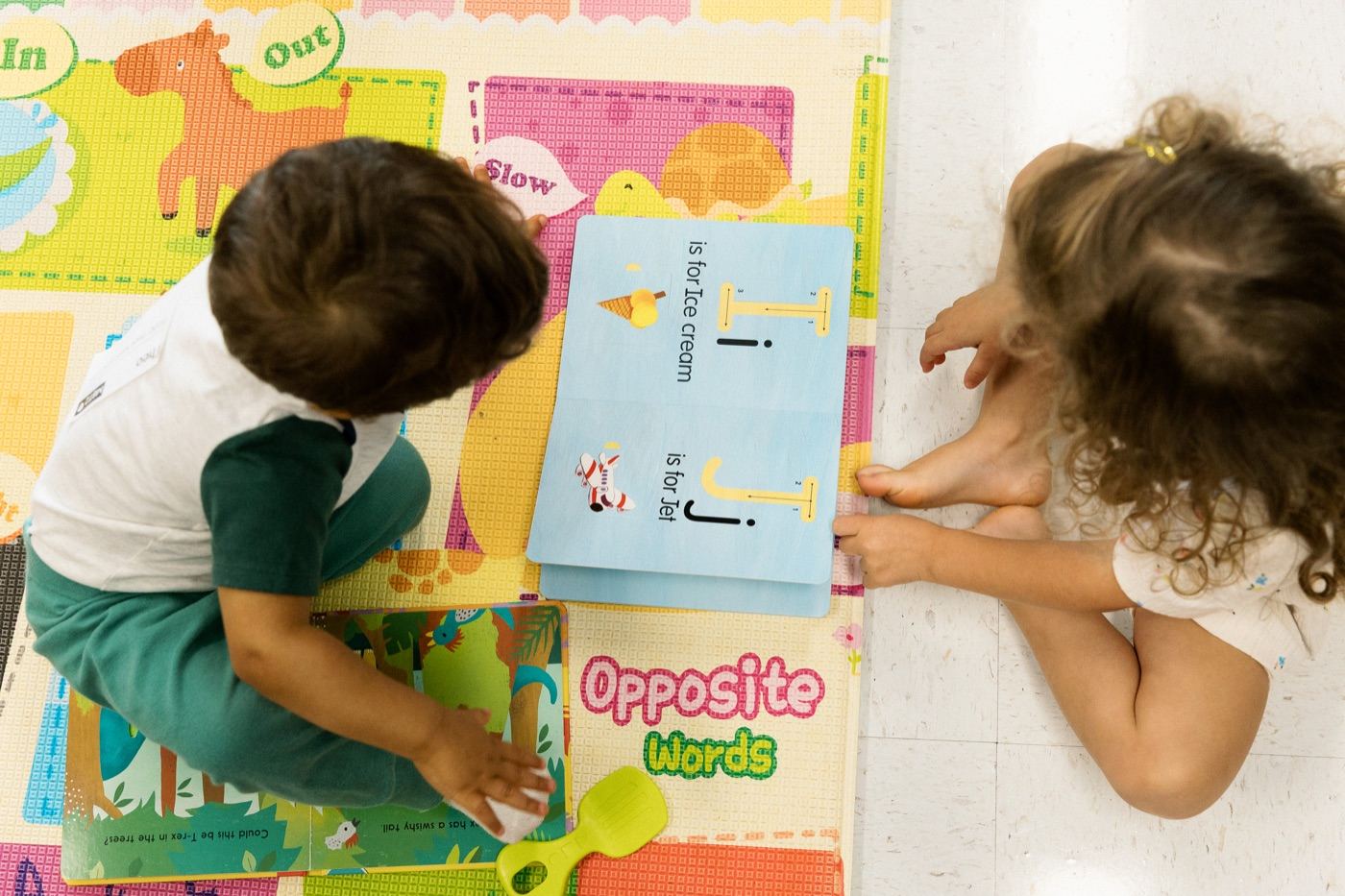 Two toddlers looking at alphabet learning cards together on the nursery play mat