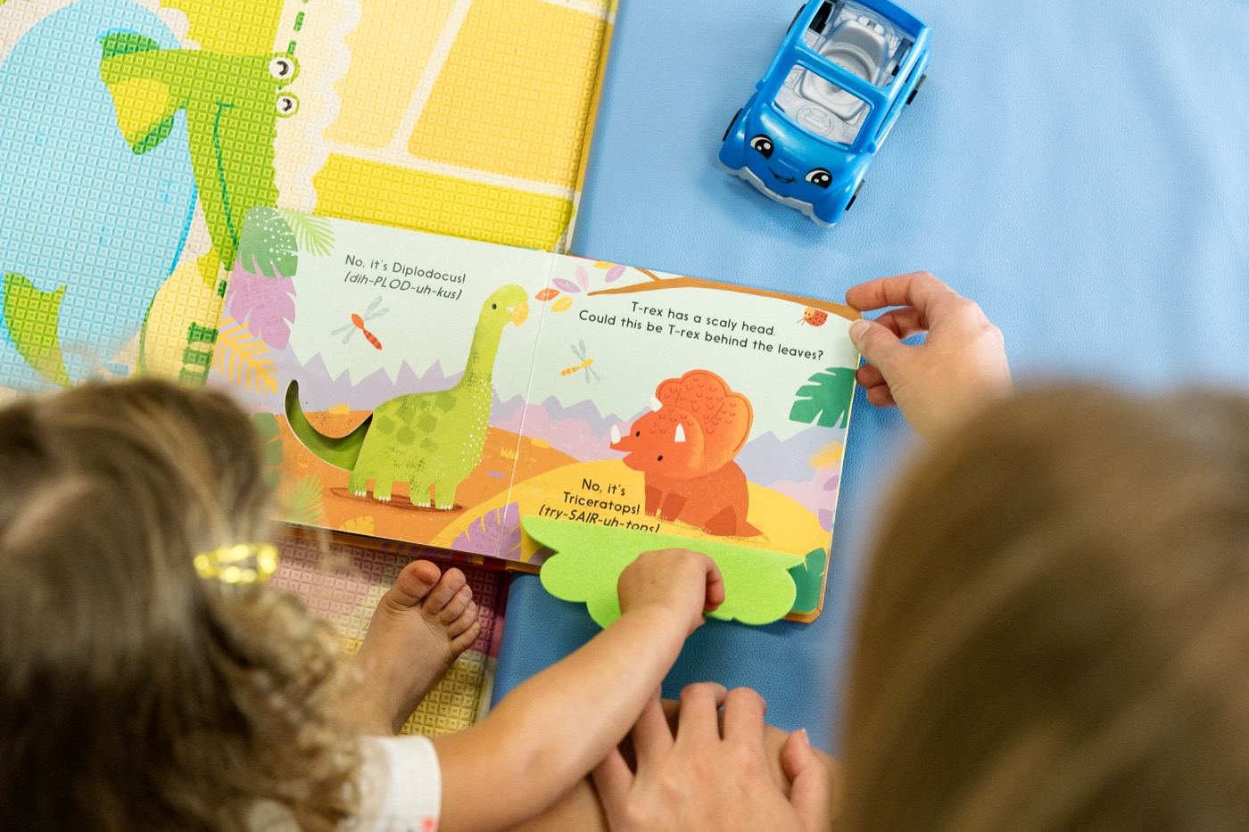 Two children and a caregiver looking at a dinosaur board book together in the church nursery